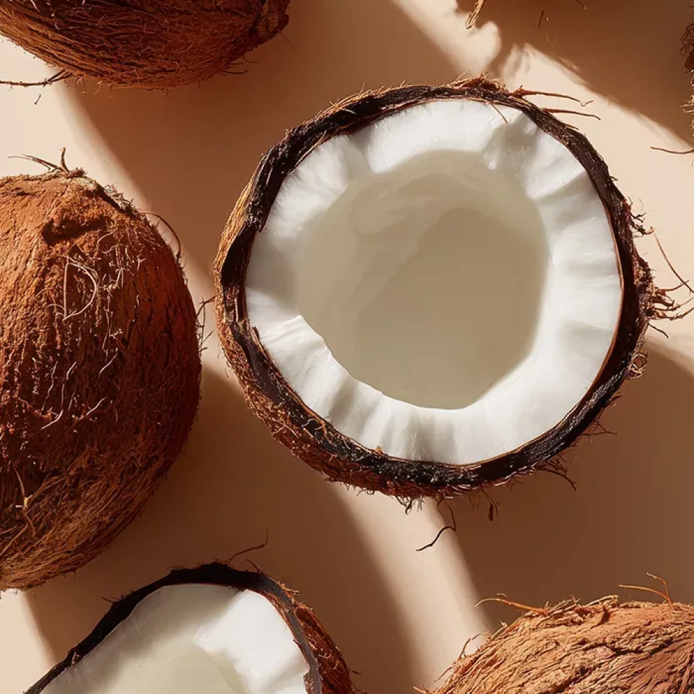 Overhead view of whole and halved coconuts with white flesh and brown husks on a beige surface.
